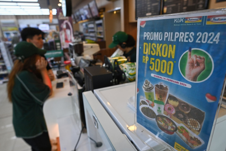 A shopkeeper serves a customer standing near a poster advertising an election day discount on Feb. 14, 2024, in a convenience store in Jakarta.