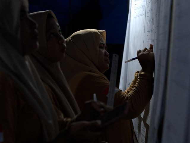 Eyestrain: Poll workers tabulate votes at dawn on Feb. 15, 2024 at a poorly lit polling station in Ranomeeto subdistrict, South Konawe regency, Southeast Sulawesi.