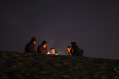 People sit by the fire at a camp for displaced Palestinians in Rafah, in the southern Gaza Strip, on the eve of the Muslim holy fasting month of Ramadan on March 10, 2024, amid ongoing battles between Israel and the militant group Hamas. 