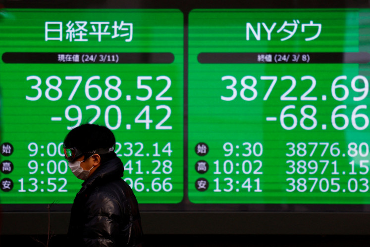A passerby walks past an electric screen displaying Japan's Nikkei share average and the Dow Jones Industrial Average outside a brokerage in Tokyo on March 11, 2024.