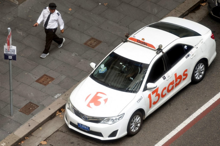 A taxi driver walks past a taxi parked in central Sydney on March 18, 2024. Australian taxi drivers impacted by the rise of ridesharing giant Uber have won US$178 million in compensation, lawyers said on March 18 after settling a gruelling legal battle. 