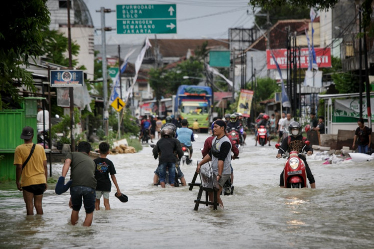 People wade across a flooded street after heavy rains in Demak, Central Java, on March 16, 2024. 