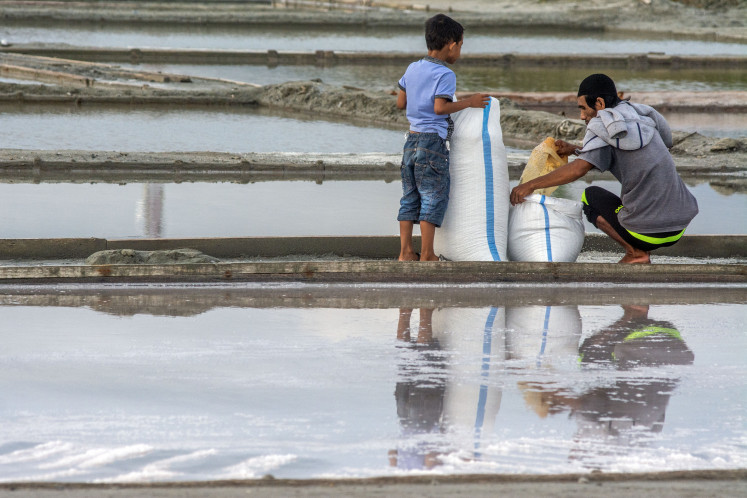 A boy helps a salt farmer harvest the mineral on March 17, 2024 in the coastal subdistrict of Talise in Palu, Central Sulawesi.