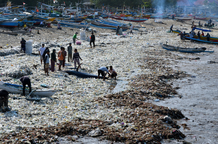 People walk along the trash covering Kedonganan Beach in Badung, Bali, on March 20, 2024.