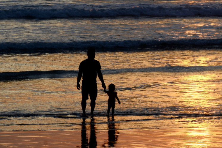 A father and a child watch as the sun sets on Sept. 6, 2021, at Kuta Beach in Badung regency, Bali.