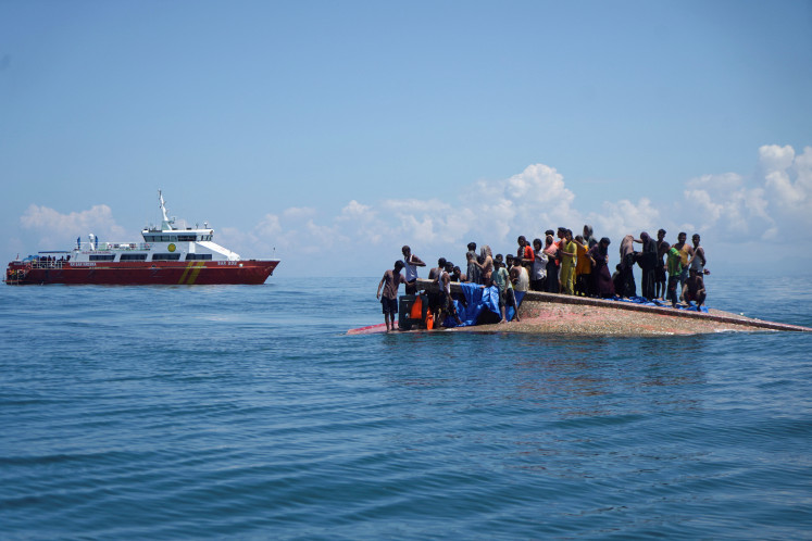 Rohingya people remain sit atop their overturned boat on March 21, 2024, in the waters off Meulaboh, West Aceh, Aceh. Local authorities rescued 69 Rohingyas from the vessel, including 24 women, whose intended destination remains unknown.