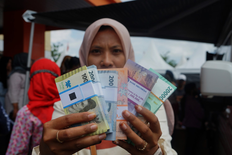 A woman displays new rupiah bills at a money exchange counter in Lembupeteng sports hall, Tulungagung, East Java, on March 28, 2024. 