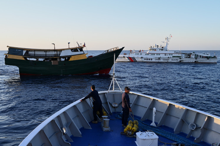 A China Coast Guard vessel (back right) sails on March 5, 2024, near the Philippine military-chartered Unaizah May 4 (left) during its supply mission to Second Thomas Shoal in the disputed South China Sea. 