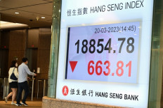 People walk past a sign showing the numbers for the Hang Seng Index in Hong Kong, China, on March 20, 2023.
