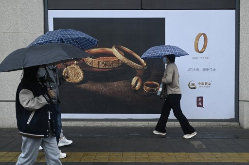 People holding umbrellas walk past a gold advertisement on a rainy day in Beijing on April 10, 2024.