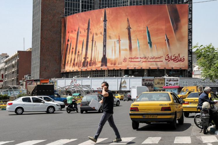 A man walks across a pedestrian crossing near a billboard depicting named Iranian ballistic missiles in service, with text in Arabic reading “the honest [person's] promise“ and in Persian “Israel is weaker than a spider's web“, in Valiasr Square in central Tehran on April 15, 2024. Iran on April 14 urged Israel not to retaliate militarily to an unprecedented attack overnight, which Tehran presented as a justified response to a deadly strike on its consulate building in Damascus.