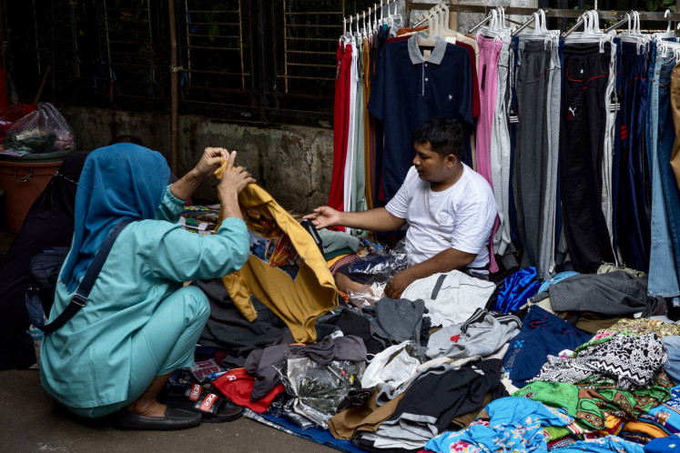 A woman chooses clothes to purchase from a street vendor at a traditional market in Jakarta on April 2, 2024. 