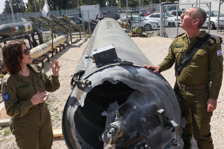 Israeli military spokesman Rear Admiral Daniel Hagari (right) and his deputy Masha Michelson pose next to an Iranian ballistic missile which fell in Israel on the weekend, during a media tour at the Julis military base near the southern Israeli city of Kiryat Malachi on April 16, 2024. 