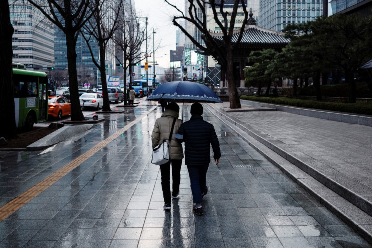 A couple share an umbrella during light rain as they walk along a street in Seoul on March 12, 2024.