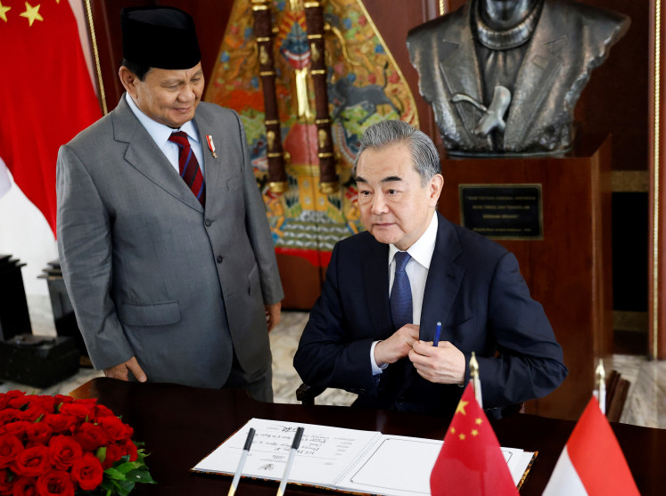 Chinese Foreign Minister Wang Yi sits after signing the guest book as Indonesia’s Defense Minister and president-elect Prabowo Subianto stands next to him, during their meeting in Jakarta, on April 18, 2024.