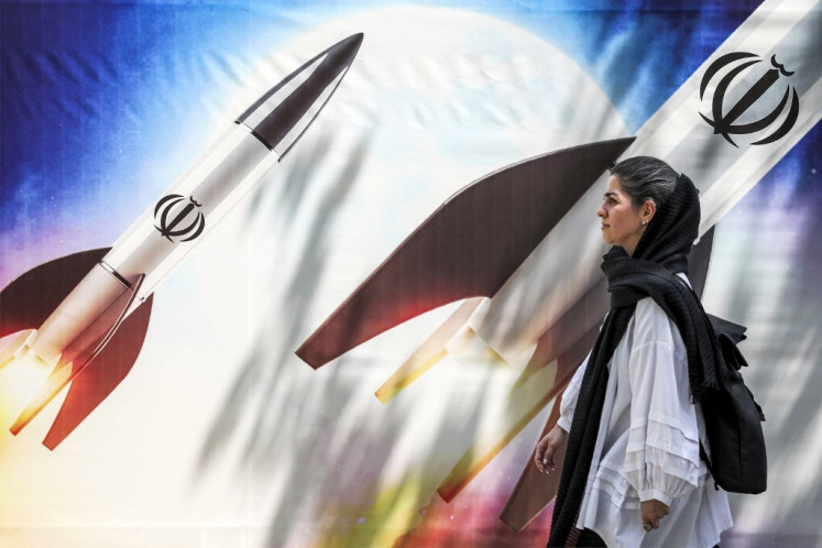 A woman walks past a banner depicting launching missiles bearing the emblem of the Islamic Republic of Iran in central Tehran on April 15, 2024. 