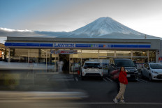 A tourist poses in front of a convenience store on January. 1, 2024, with Mount Fuji in the background, in the town of Fujikawaguchiko, Yamanashi prefecture, Japan. A huge black barrier to block Mount Fuji from view will be installed in a popular photo spot by Japanese.