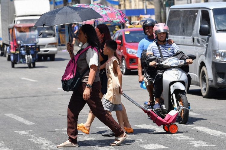 A family holding umbrellas to protect themselves from the sun walk across a street in Manila on April 25, 2024. Extreme heat is scorching parts of South and Southeast Asia, prompting health warnings from authorities as high temperatures are recorded across the region.