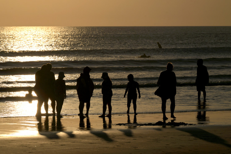 People enjoy a sunset at Kuta beach near Denpasar, Bali, on April 15, 2024.