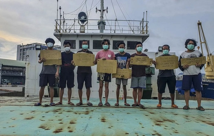 Calling home: Indonesian fishers hold posters on Aug. 11, 2022, aboard a vessel as it docks at Kaohsiung Port in Taiwan, asking for the government’s help to repatriate them. The fishermen were reportedly stuck on the boat, believed to belong to a Hong Kong company, since February 2022 without pay.