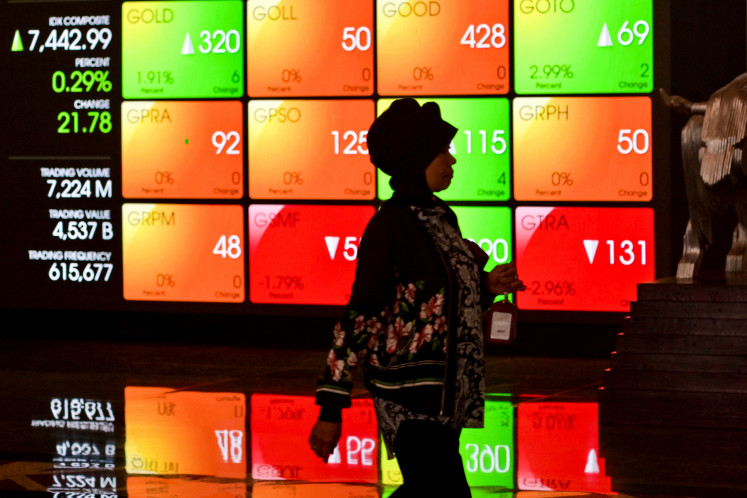 A woman walks past a large screen displaying stock indices on March 14, 2024, at the Indonesia Stock Exchange (IDX) in Jakarta. The IDX Composite dipped by 0.17 percent to 7,123.61 following fluctuations on, May 7, 2024.