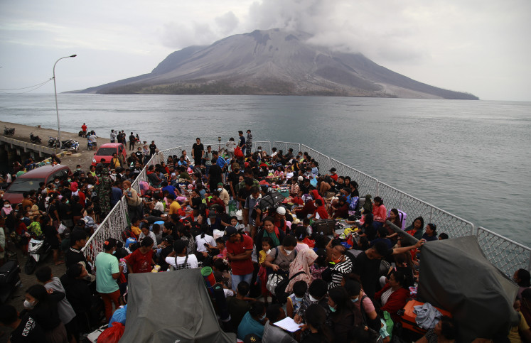 Some 330 residents evacuated from Sitaro Islands regency, North Sulawesi, amid the eruption of Mount Ruang (background) leave Tagulandang on May 1, 2024, for Bitung aboard the Indonesian Navy’s KRI Kakap.