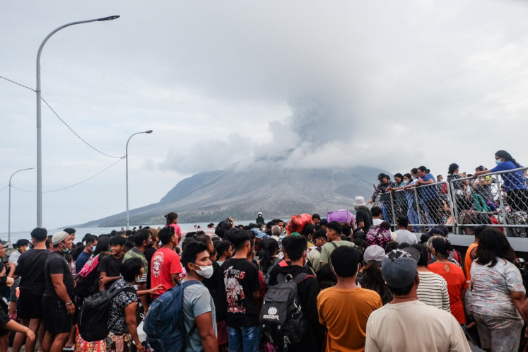 Evacuees board a naval vessel on Tagulandang Island in Sitaro, North Sulawesi on May 1, 2024, as Mount Ruang volcano spews smoke in the background. 