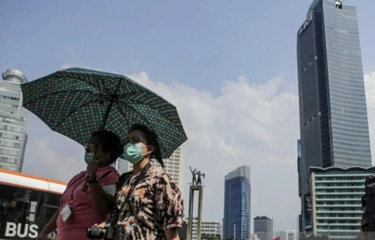 Jakarta residents walk under sun heat at the Hotel Indonesia traffic circle in Jakarta on April 24, 2023.