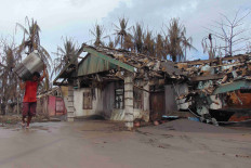 A person carries his belongings as he walks past a damaged house affected by the eruption of Mount Ruang volcano in Laingpatehi village, Sitaro Islands Regency, North Sulawesi, May 3, 2024. 