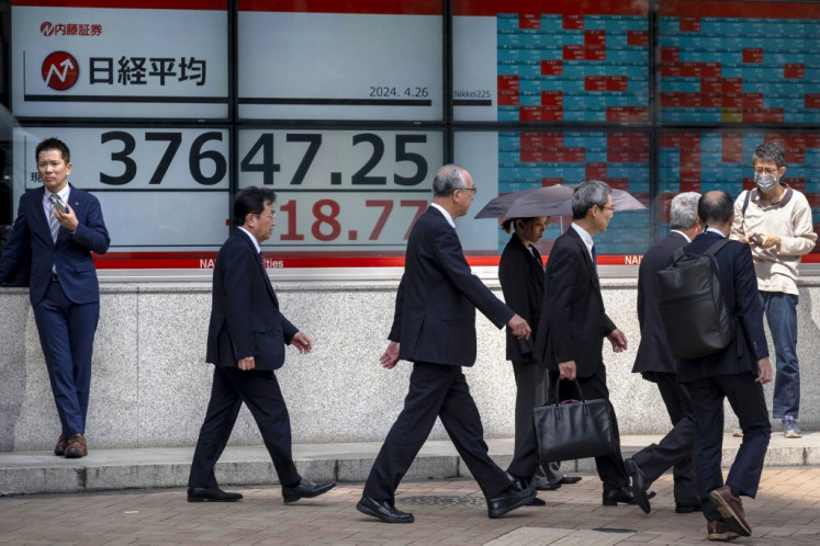 People walk in front of an electronic board displaying the latest reading of the Nikkei index of the Tokyo Stock Exchange on a street in Tokyo on April 26, 2024.