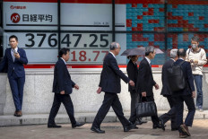 People walk in front of an electronic board displaying the latest reading of the Nikkei index of the Tokyo Stock Exchange on a street in Tokyo on April 26, 2024.