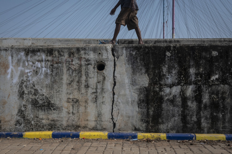A person walks on a cracked sea wall on May 7, 2024, in Kalibaru, Cilincing, North Jakarta. Residents of the
area fear that the wall, which was built to protect the area from
the waves and tide, could collapse at any time.