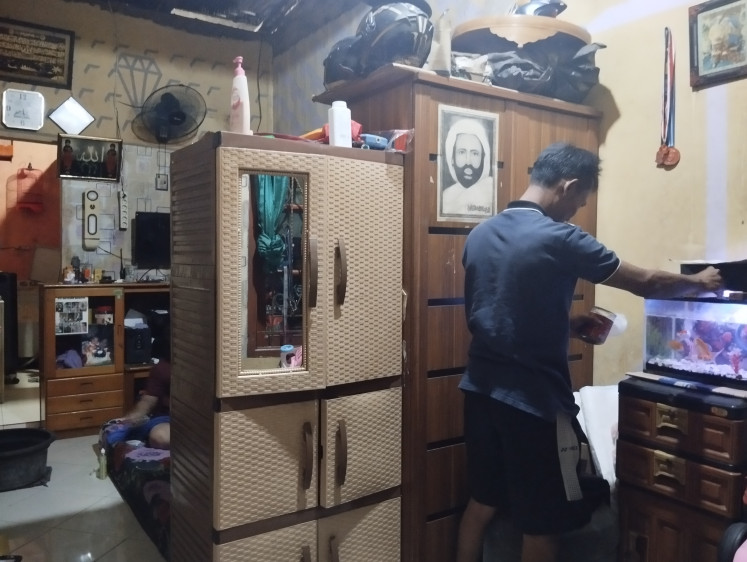 Hendra feeds fish in his small house in Jembatan Besi, Tambora, West Jakarta, on April 17, 2024 while his wife is folding clothes on the bed, behind the cupboard. People who reside in densely populated settlements live with limited space. 