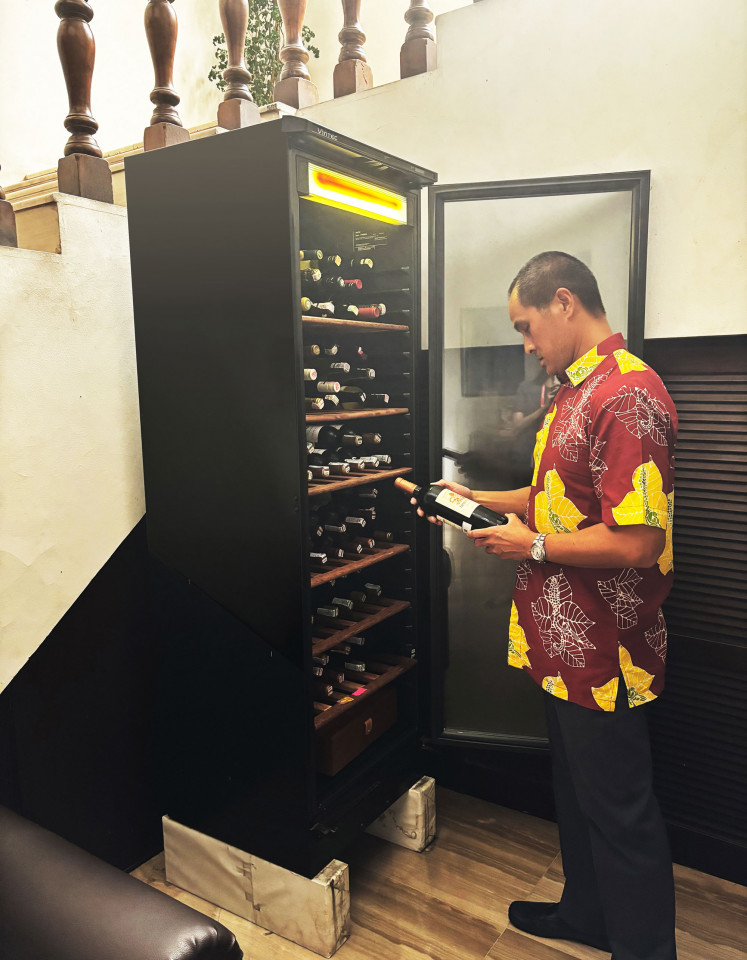 Luki Wanandi inspects a wine bottle from his chiller at his office, part of his collection. 