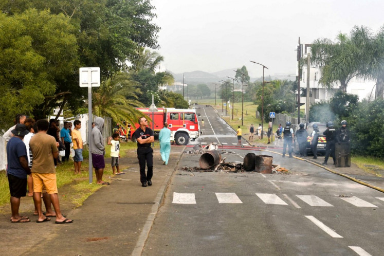 People, French gendarme officers and firefighters stand near temporary burning roadblock set up by demonstrators in Noumea on May 14, 2024, amid protests linked to a debate on a constitutional bill aimed at enlarging the electorate for upcoming elections of the overseas French territory of New Caledonia. 