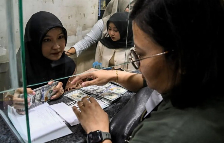 A teller (left) serves a customer at a money exchange in Jakarta on April 17, 2024.