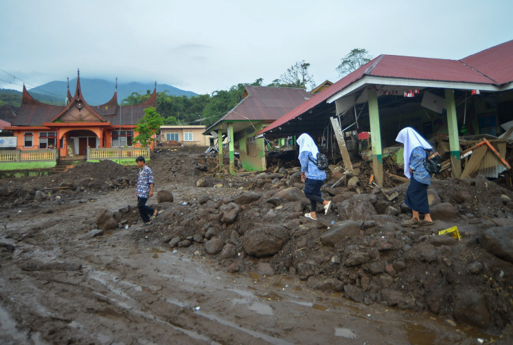 Two uniformed students walk atop rubble on May 15, 2024 past a collapsed school in Agam, one of the regions that were worst affected when flash floods and lahars struck West Sumatra on May 11.