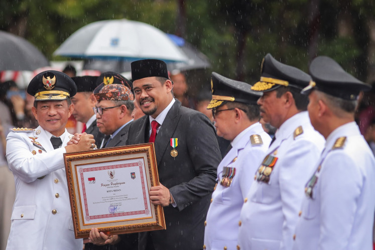 Home Minister Tito Karnavian (left) gives an award to Medan Mayor Bobby Nasution (second left) on April 25, 2024, during a ceremony at the Surabaya town hall commemorating regional autonomy.