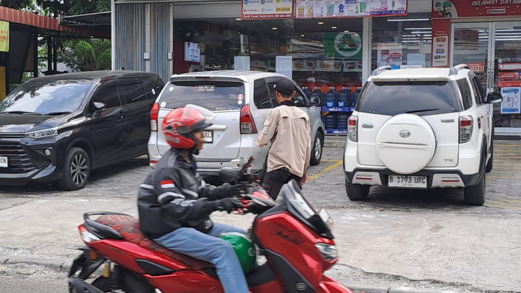 A motorcycle passes by as parking attendant Muhammad “Didin” Fachruddin directs a car that is about to get out of the Alfamidi parking lot in South Jakarta on May 24, 2024.