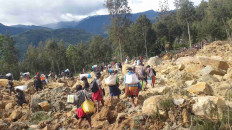 People carry bags in the aftermath of a landslide in Enga Province, Papua New Guinea, May 24, 2024, in this still image obtained from a video. 
