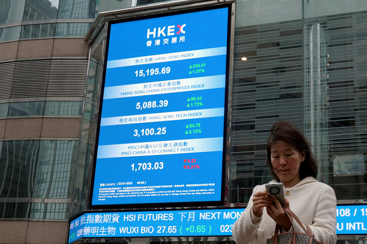 A woman checks her mobile phone near screens displaying the Hang Seng stock index and stock prices outside the Exchange Square in Hong Kong, China, on Jan. 23, 2024.