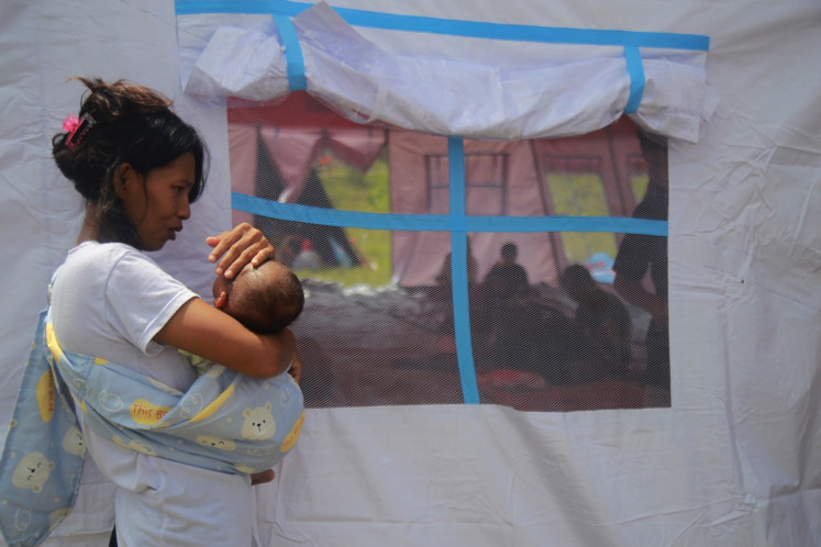 A woman carries her infant on May 18, 2024 beside an emergency tent in Gam Ici village sheltering people who fled the Mount Ibu eruption in West Halmahera regency, North Maluku.