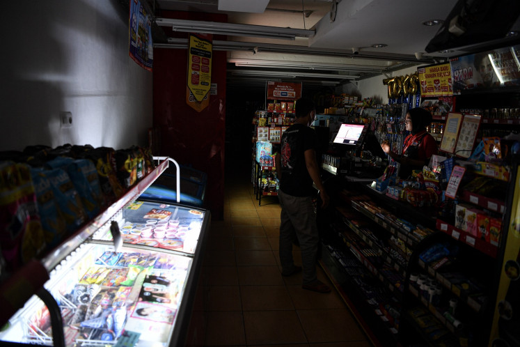 A convenience store worker serves a customer in Palembang, South Sumatra, on June 4, 2024, during a blackout affecting regions across Sumatra. State electricity company PLN blamed the blackout on a disruption on a high-voltage power line in South Sumatra.