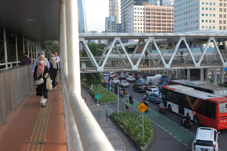 Several office workers wear mask while walking on a pedestrian bridge at Jl. Sudirman in Jakarta on June 7, 2024.