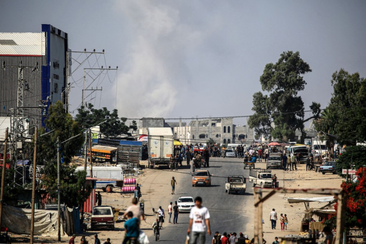 Palestinians pursue their daily chores, as smoke rises following the Israeli bombardment of the city of Rafah, in the southern Gaza Strip on June 11, 2024, amid the ongoing conflict between Israel and the Hamas militant group. 