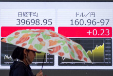 A woman walks past electronic boards displaying the exchange rate for the Japanese yen against the US dollar and the Nikkei index of the Tokyo Stock Exchange in Tokyo on June 28, 2024.