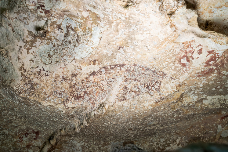 A painting created at least 51,200 years ago in the limestone cave of Leang Karampuang in the Maros-Pangkep region in Sulawesi portrays three human-like figures interacting with a wild pig, in this undated handout image. 