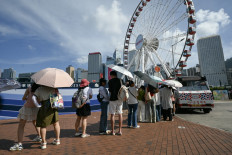 Tourists use umbrellas to protect themselves from the sun as they queue to buy ice cream from a truck near Victoria Harbour in Hong Kong, China, on July 8, 2024.
