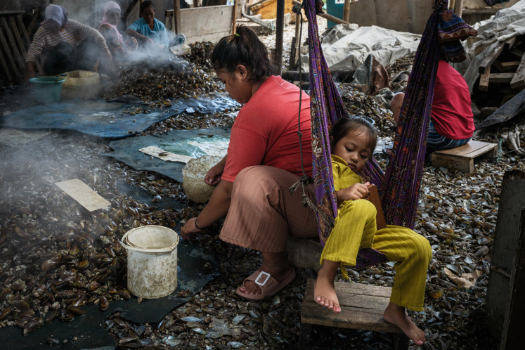 A woman removes boiled green mussels from their shells beside her daughter in a fishing community in North Jakarta on March 19, 2024.
