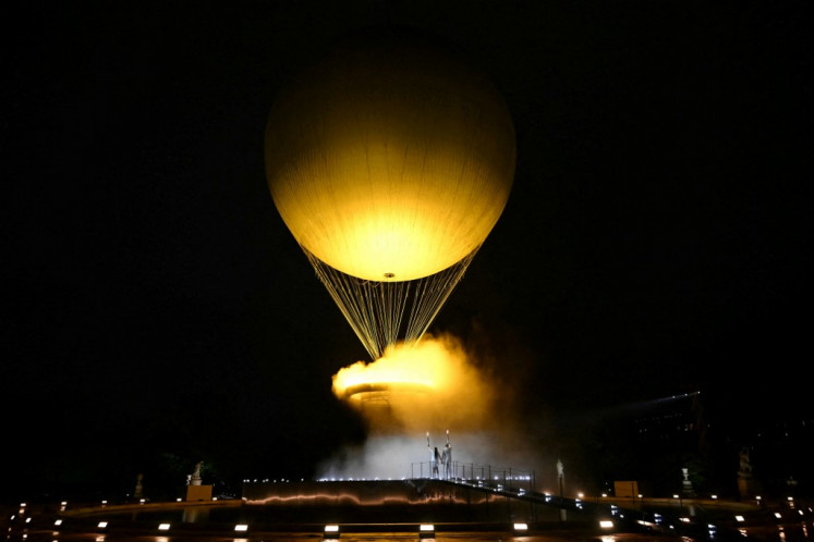 The cauldron, with the Olympic flame lit, lifts off while attached to a balloon as the torchbearers French former sprinter Marie-Jose Perec and French judoka Teddy Riner stand in front during the opening ceremony of the Paris 2024 Olympic Games at the Jardin des Tuileries (Tuileries Garden) in Paris on July 26, 2024.